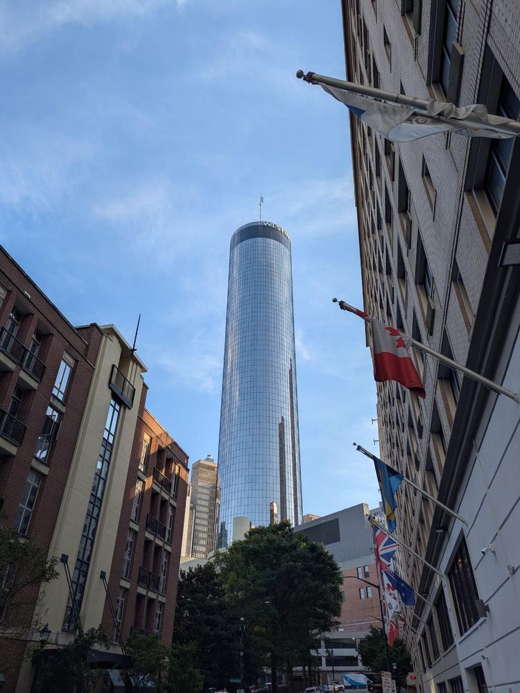 Day time blue sky with some thin wispy clouds and a mirror finish tall totally cylindrical skyscraper (Westin - large letters on top)