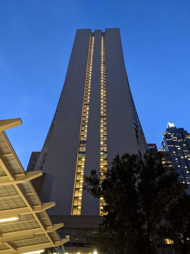 Dusk, almost night view of a tall building rectangular profile with a curved wider bottom portion and two columns of windows all lit going up the building