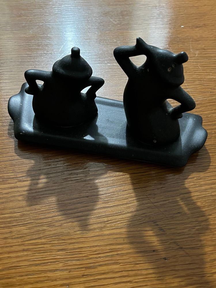 Pottery salt and pepper shakers that are vogue-ing, with arms akimbo; glazed in flat black on an asymmetric flat pottery tray.  