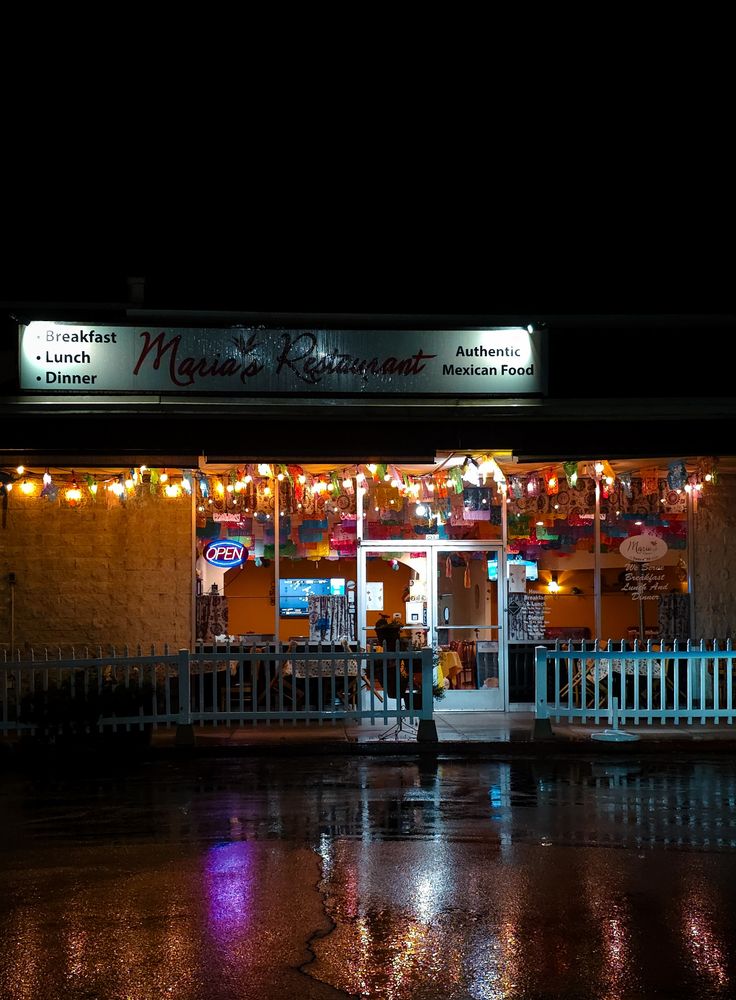 Night-shot image of a warmly lit, cozy  restaurant on a cold, rainy evening. The lights cast an inviting glow across the wet pavement outside. 