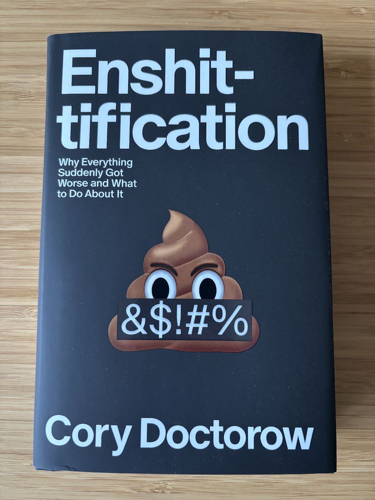 Hardcover book with a poop swearing emoji on a black background. The book is Enshittification: Why Everything Suddenly Got Worse and What to Do About It by Cory Doctorow.