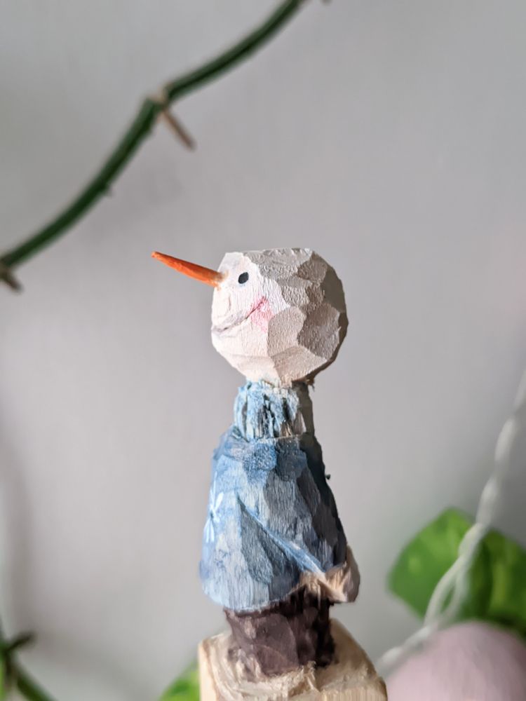 A profile view of wood carved snowman.
A carrot nose, rosy cheeks and a blue jumper. 
On the other profile, you would see that he is missing a hand that I unfortunately cut off while trying to give a better shape to  the arm. Oops! 