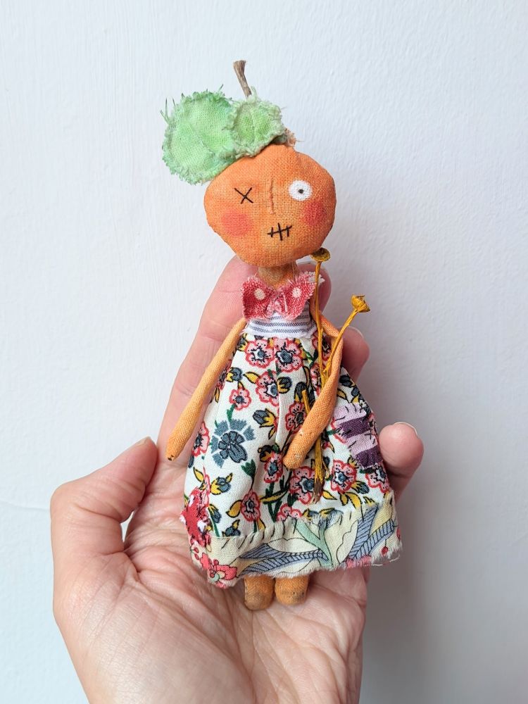 A hand holding a little textile pumkin doll wearing a pretty dress. 