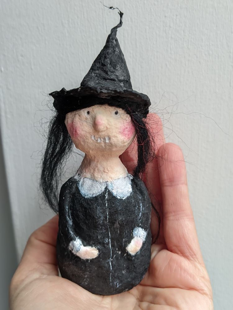 A hand holding a little spun cotton doll featuring a little witch. 