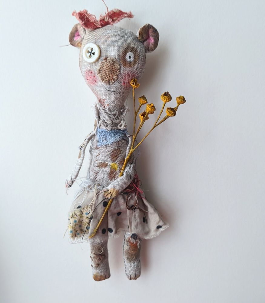 A perfectly imperfect bear made of grey linen holding flowers. 