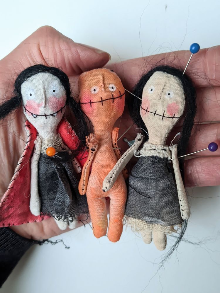 Three mini rag dolls held by an open hand.
One little vampire girl, an orange character (future pumpkin doll) and a black hair girl (future witch). 