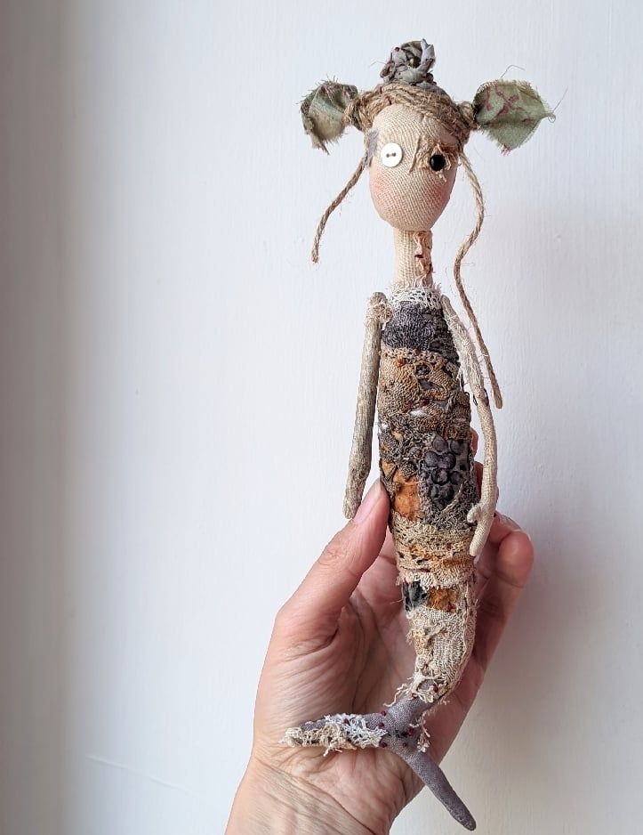A hand holding a mermaid textile doll. 