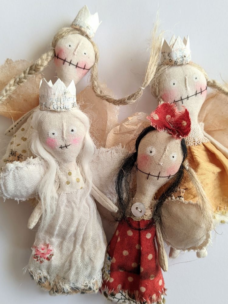 A bunch of small textile dolls with wings.
One red dress, one white dress and two f9lden dress at the back. 