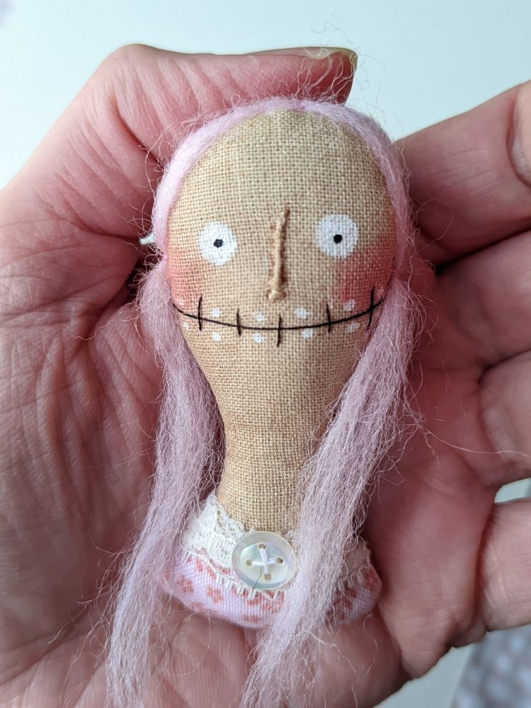A hand holding a pink hair girl head made of fabric. 
