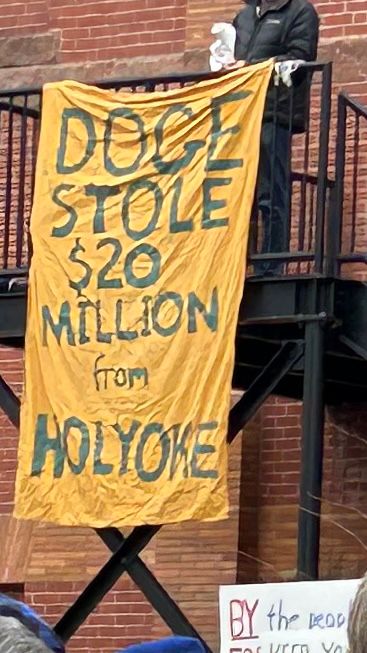 A photo of a sign at the Northampton Resists Together protest today in Massachusetts. It is green writing on a yellow flag and says “DOGE stole 20 million from Holyoke.” Holyoke is a deindustrialized Puerto Rican majority city in Western Massachusetts. 
