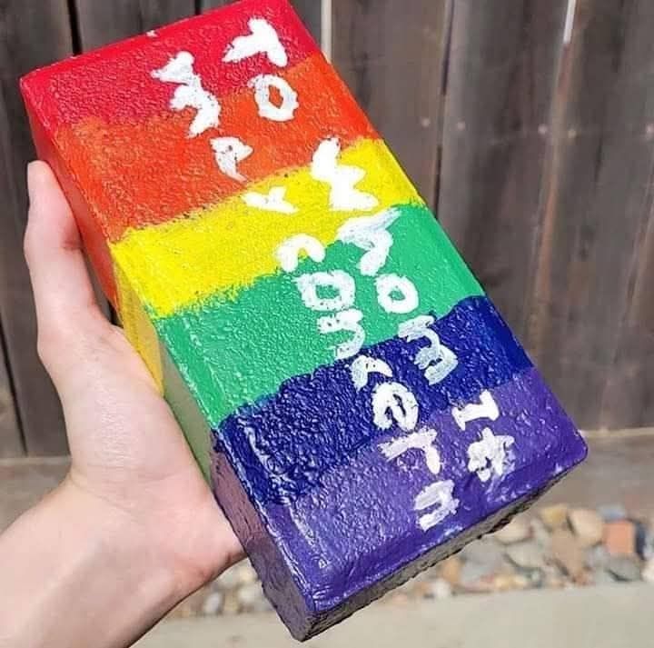Hand holding a rainbow brick with the text "to whom it may concern" painted on it. 