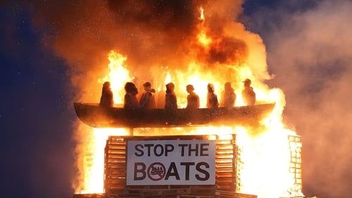 A burning boat filled with effigies of refugees burns on a celebratory cultural heritage bonfire in Northern Ireland, famously welcoming to all, except if you're going to the British Open golf next week, watch out for the marchers, who won't change their timing, presumably because they were there first