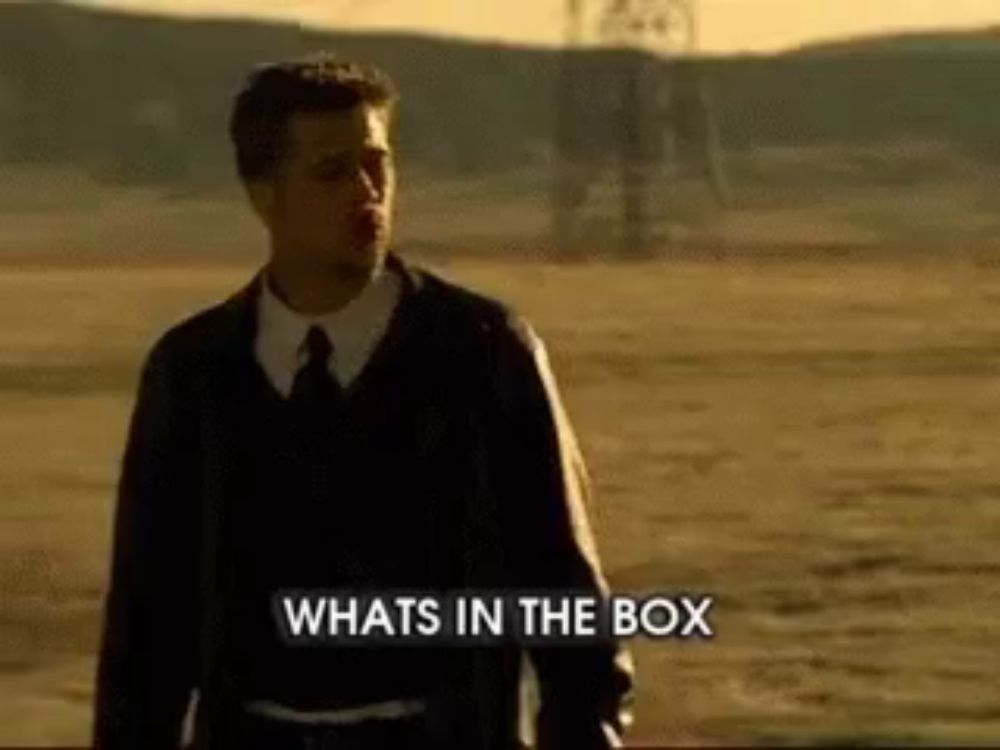 a man in a suit and tie is standing in a field with the words whats in the box behind him