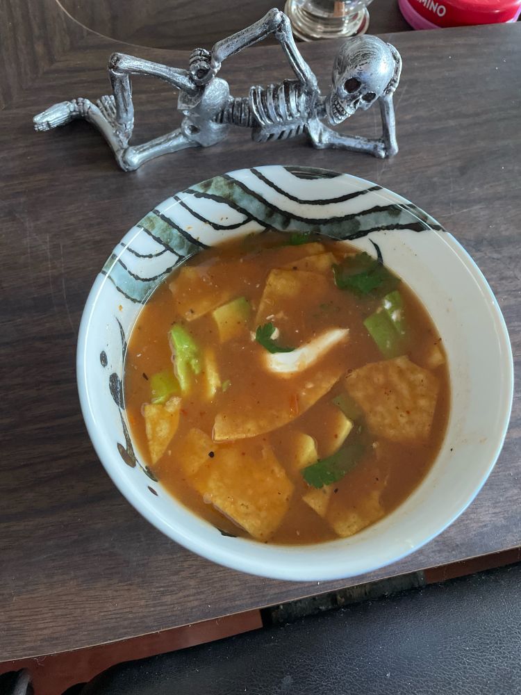Bowl with red soup with tortilla chips, avocado, cilantro and creama