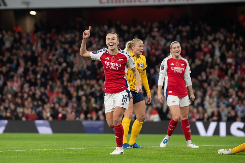 Caitlin Foord of Arsenal Women celebrates scoring a goal, she is smiling and pointing to the sky.