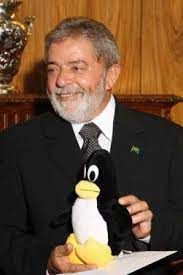 foto de uma pessoa de terno (Presidente Luis Inácio Lula da Silva) segurando com as mãos uma pelúcia de pinguim