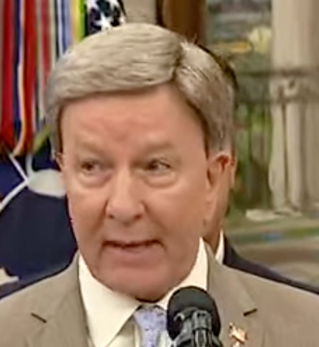 An old white guy in a tan suit with a blonde wig floating just above his head.