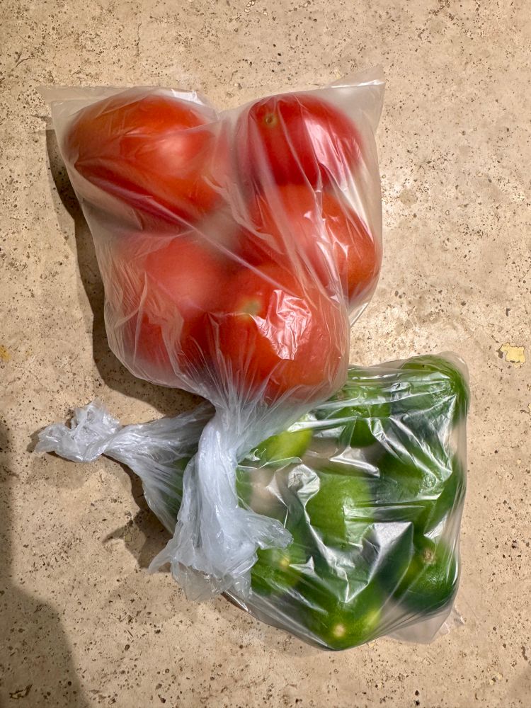 Picture of bags of fresh ripe tomatoes and limes on marble countertop. 