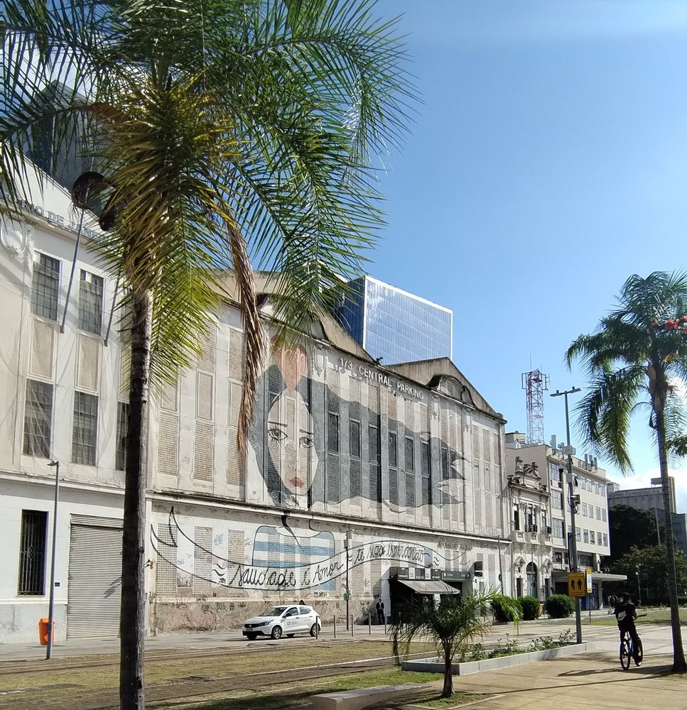 Foto tirada do calçadão do Pier Mauá. Mostra prédios com grafites, uma palmeiras e céu azul. 