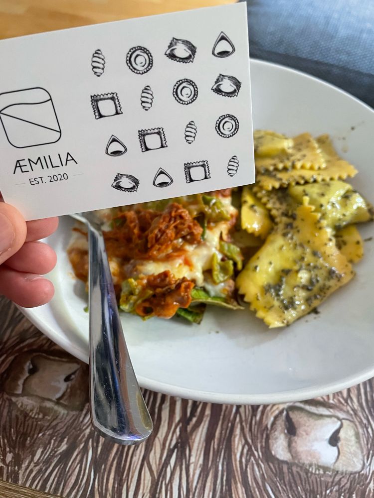 A bowl, filled with braised beef lasagne and spinach & ricotta pasta. A business card for Æmilia, the pasta shop they were bought from, is in the foreground.