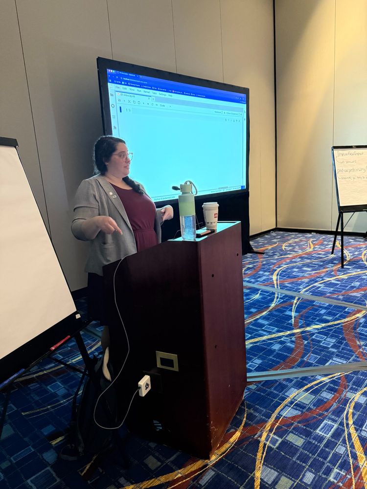 A presenter at the podium with a screen behind her. on which Python lesson material is projected. 