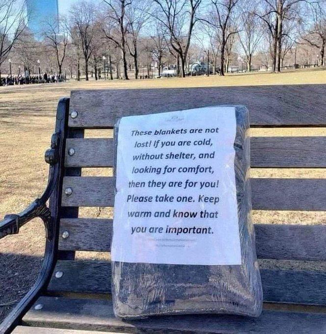 A gray blanket wrapped in plastic is sitting on a park bench.  On the front of the package is a note that says, "These blankets are not lost!  If you are col, without shelter, and looking or comfort, then they are for you!  Please take one.  Keep warm and know that you are important."