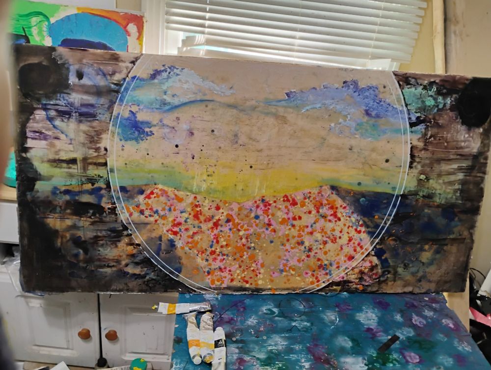 Front view of painting. ~4x2.5 foot, depicting sunrise over desert. Center focus is pulled by two concentric white circles isolating a dip in sand dunes. Sand dunes are represented by red, pink and orange dots layered on top of pale yellow/beige sand. The sky is skin toned with highlights of yellow and green sunrise. Clouds are present and partially decomposed by paint removal. Exterior of circles is obscured by smooth layers of dark tones. Painting has feelings of anxiety.