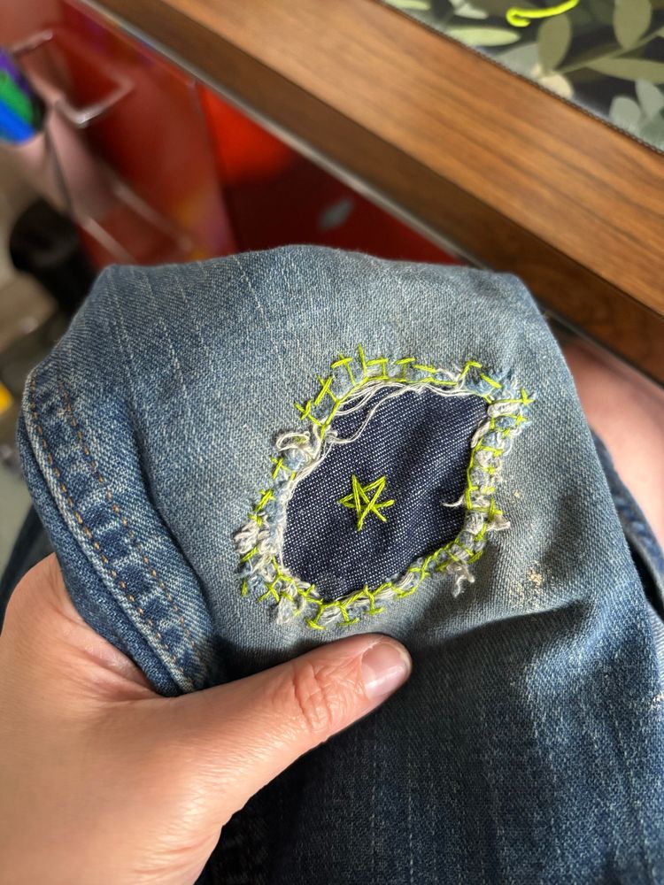 Jeans with a patch and green mending around, star in middle of patch 