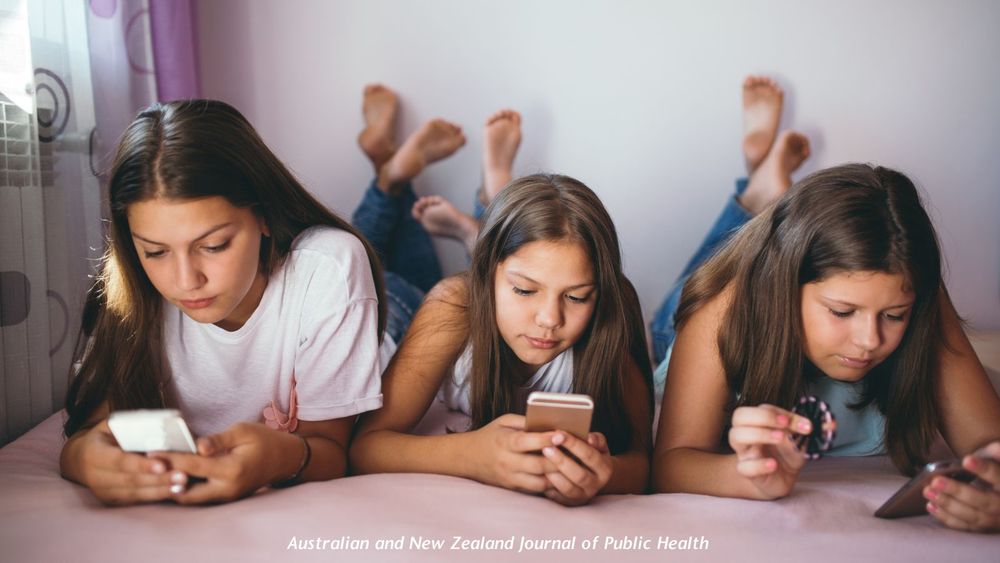 Image of three young girls lying on their stomachs in a bed reading on their phones. Text "Australian and New Zealand Journal of Public Health"