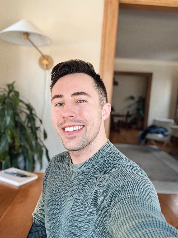 Man taking selfie smiling at camera wearing a knitted gray-green sweater