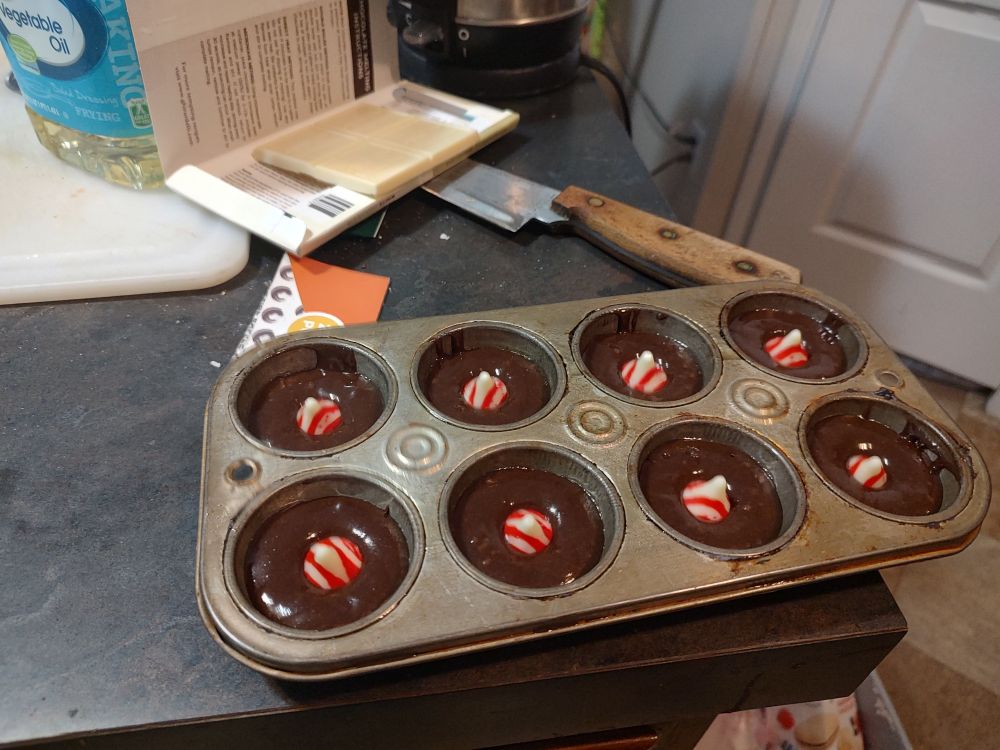 A picture of a mini muffin pan filled with brownie batter. In the middle of each brownie is a peppermint kiss