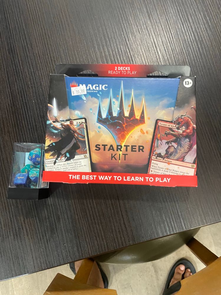 A Magic the Gathering starter kit and acrylic box of polyhedra die sitting on a table