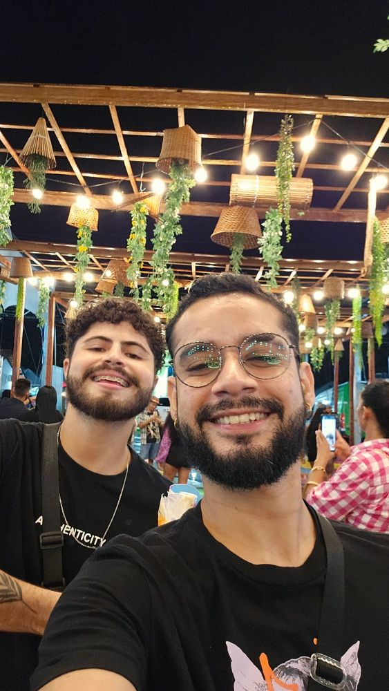 Dois namorados lindos sorrindo pra selfie com um fundo iluminado.