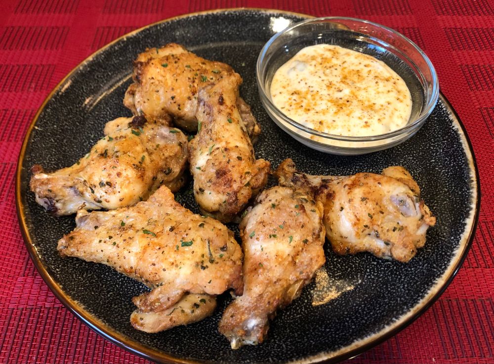 Photo of Old Bay wings, on a black plate, on a red placemat. There’s a side dipping sauce 