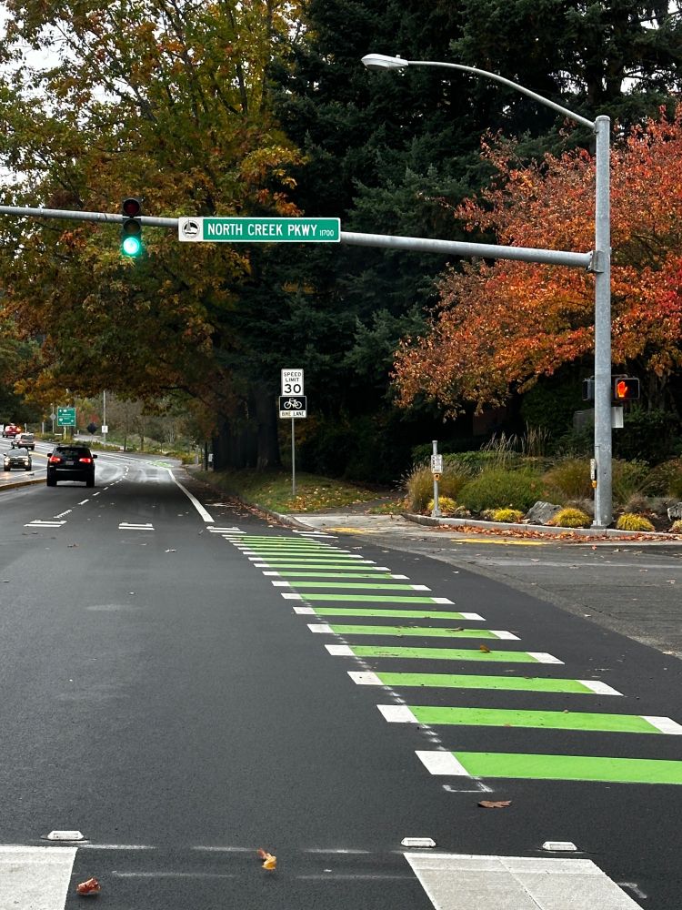 Fall foliage next to a new, painted green crosswalk for bikes underneath a road sign that says North Creek Parkway