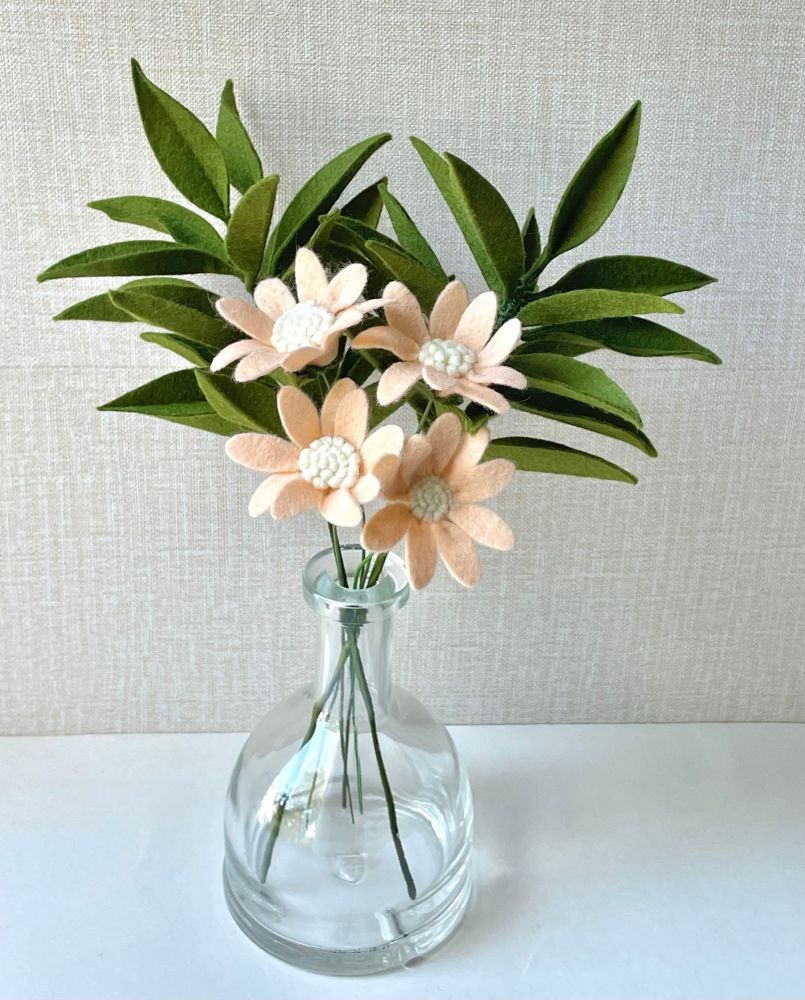 Two green felt leafs stems & four blush peach felt flowers with white centers in a clear vase. 
