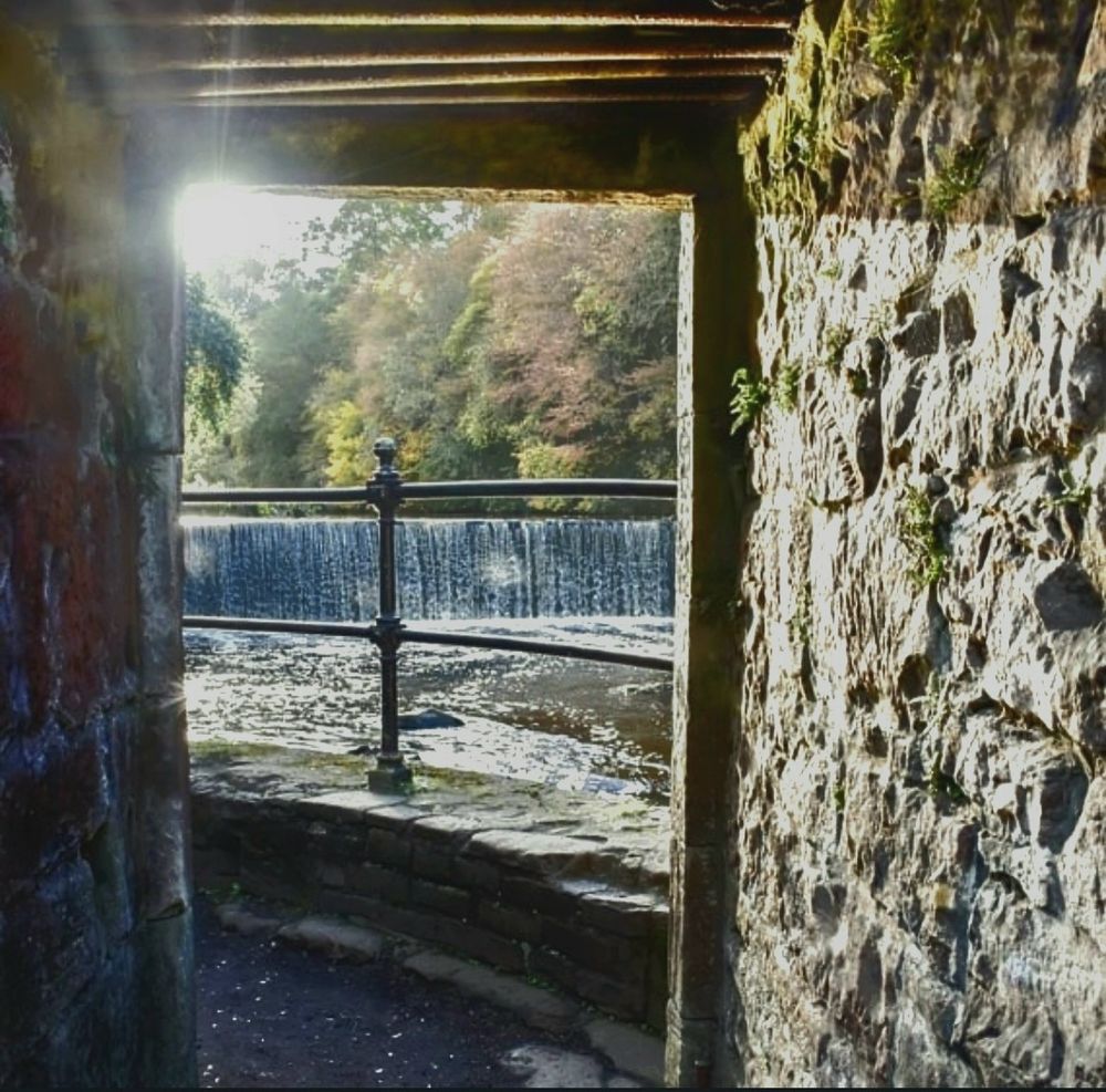 Old stone tunnel leading to a path beside a waterfall on a warm summer's evening.