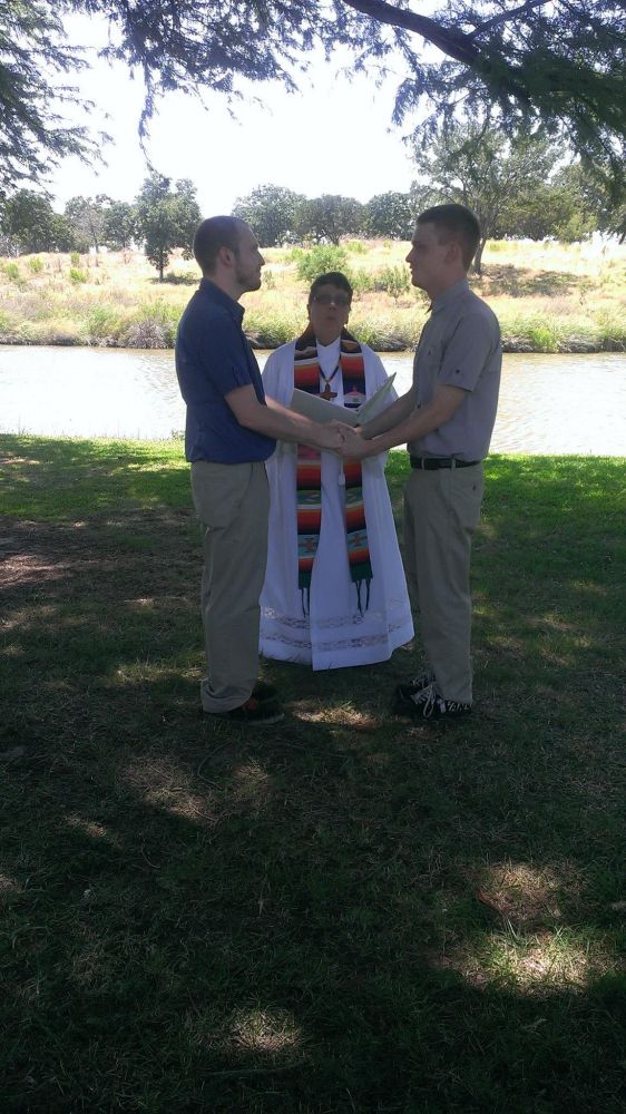 A wedding photo of my husband and I standing in front of the priest saying our vows.
