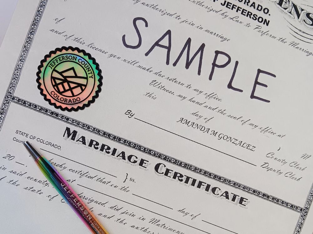 A Jeffco marriage license with a rainbow seal and a rainbow pen