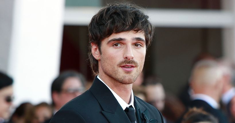 L’acteur Jacob Elordi en costume noir sur un tapis rouge, regardant vers la caméra, entouré d’autres personnes floues en arrière-plan.