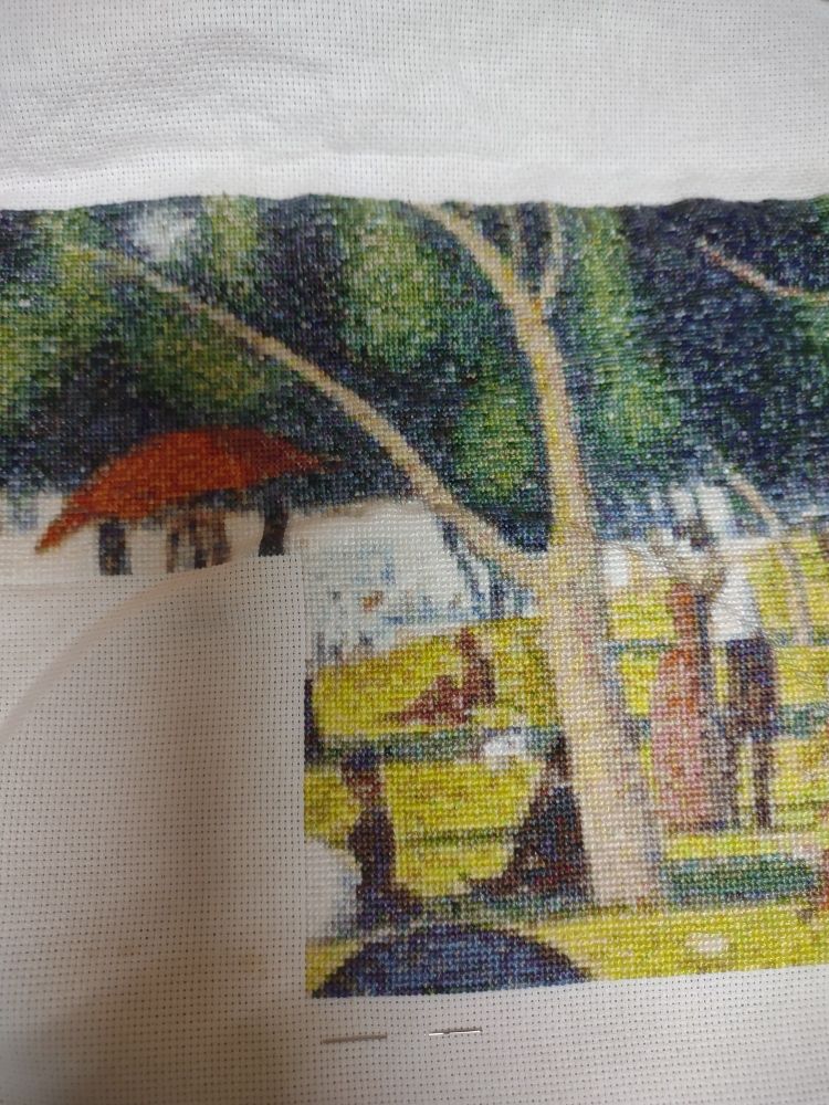 Close up of a cross stitch project showing trees with people lounging about.
