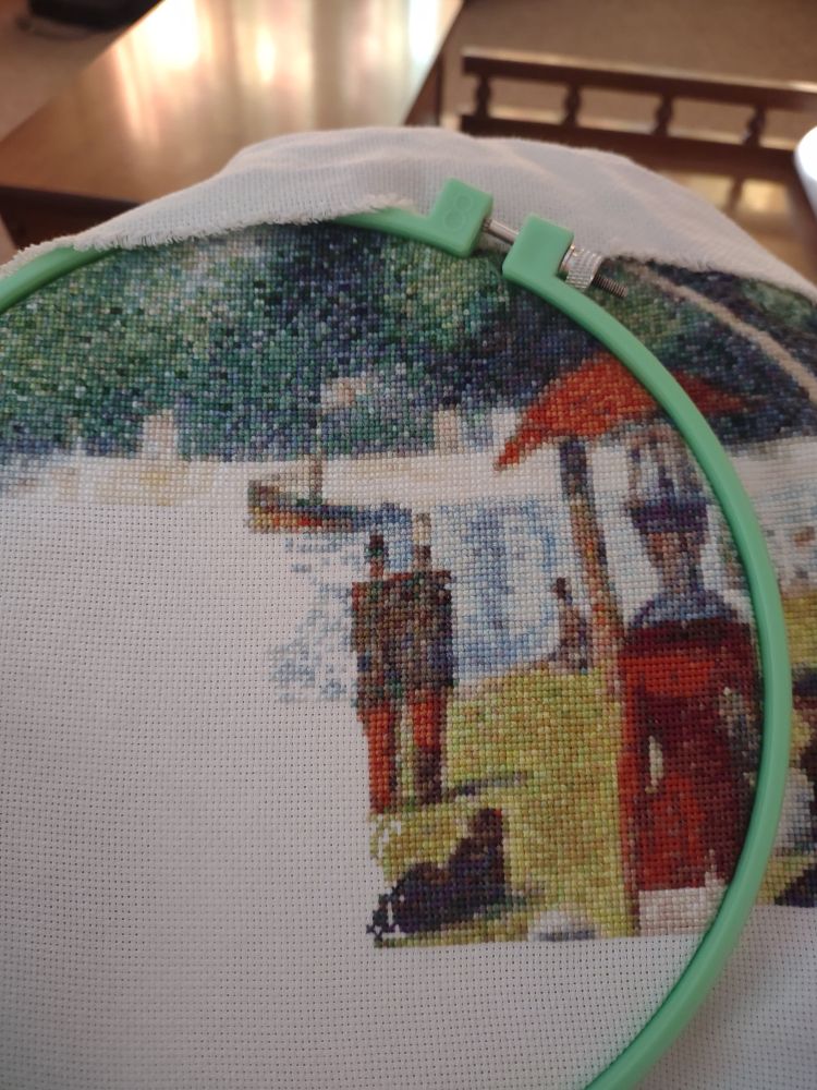 Green embroidery hoop. Scene shows a park with people in old timey clothes enjoying a lake.