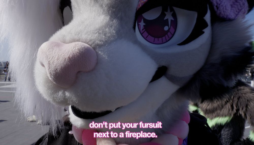a screenshot of melon wearing grape's fursuit head telling the viewer not to put their fursuit next to a fireplace