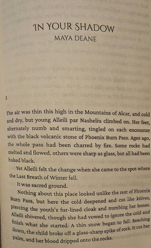 The first page of Maya Deane's "In Your Shadow": 
I. The air was thin this high in the Mountains of Alcar, and cold and dry, but young Alleili par Nasheliu climbed on. Her feet, alternately numb and smarting, tingled on each encounter with the black volcanic stone of Phoenix Burn Pass. Ages ago, the whole pass had been charred with fire. Some rocks had melted and flowed, others were sharp as glass, but all had been baked black. 
Yet Alleili felt the change when she came to the spot where the Last Breath of Winter fell. 
It was sacred ground. 
Nothing about this place looked unlike the rest of Phoenix Burn Pass, but here the cold deepened and cut like knives, piercing the youth's fur-lined cloak and numbing her bones. Alleili shivered, though she had vowed to ignore the cold and finish what she started. A thin snow began to fall. Reaching down, the child broke off a glass-sharp spike of rock. It cut her palm, and her blood dripped onto the rocks."