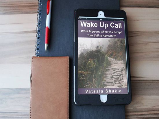 Kindle ebook, Wake Up Call: What happens when you accept Your Call to Adventure resting on notebookm with pen and glass case on table.