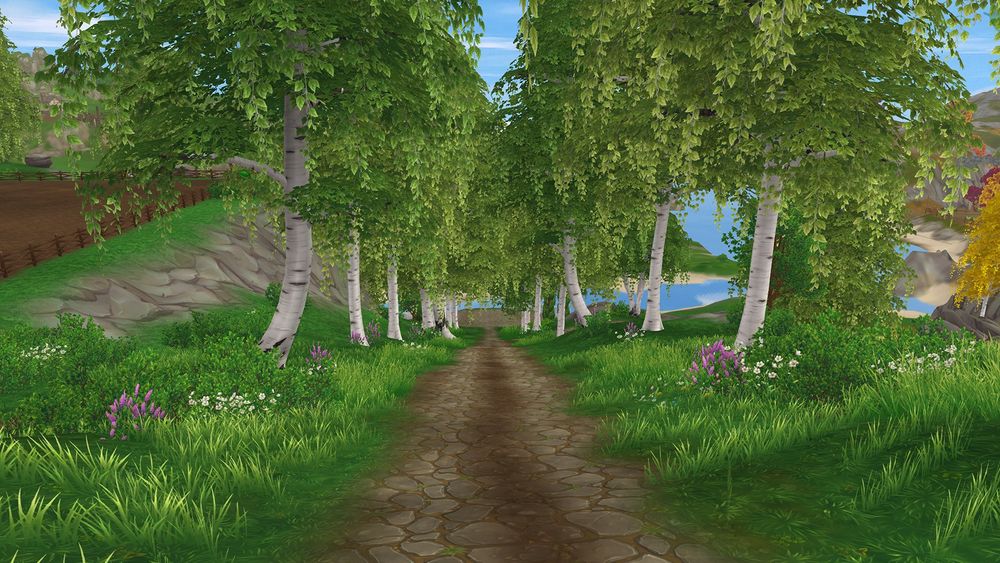A screenshot from the online game Star Stable of a cobble and dirt road lined on both sides by grass, flowers, and birch trees with draped weeping willow like branches.