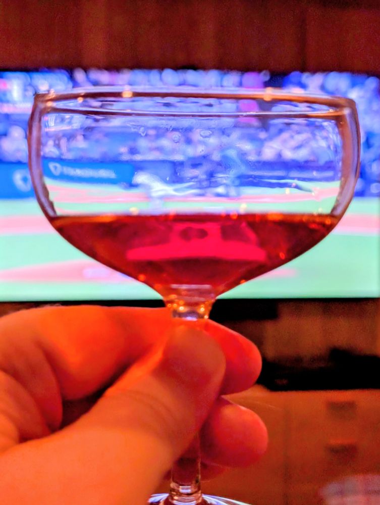 A red cocktail in a coupe, in front of a TV showing the Phillies playing the Dodgers in LA