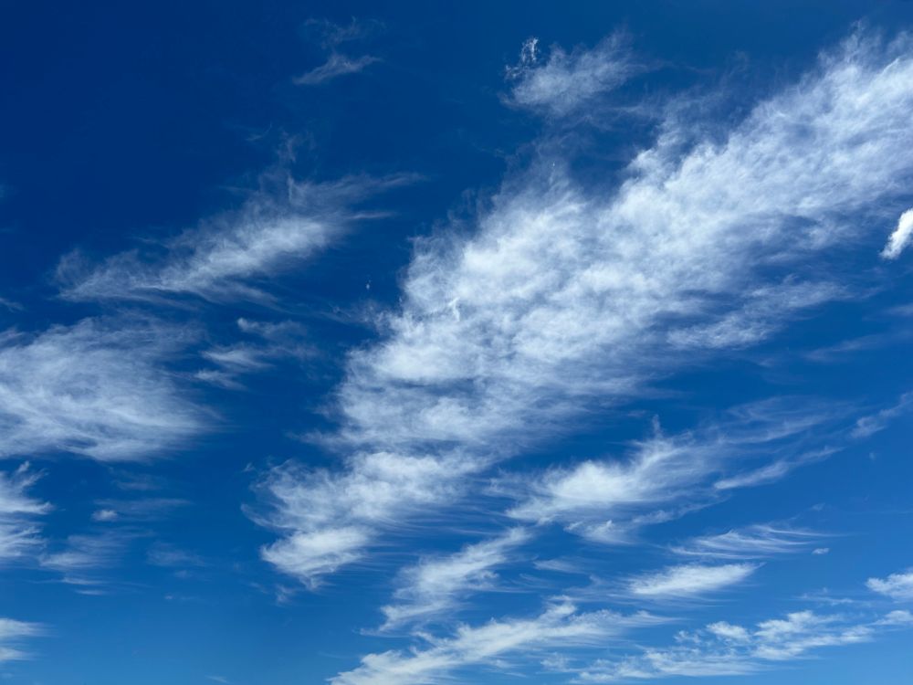 Wispy cirrus clouds stretch across a deep blue New England sky, resembling delicate brushstrokes or strands of hair.