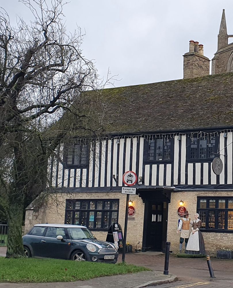 Half-timbered house, outside which stand mannequins of a man and woman in 17th-century clothing. Christmas lights are hung in the windows and along the roofline.
