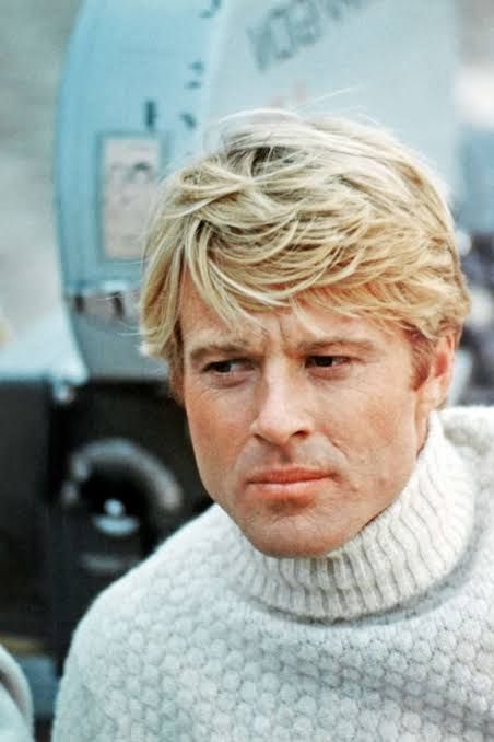 Robert Redford in sweater in front of movie camera 